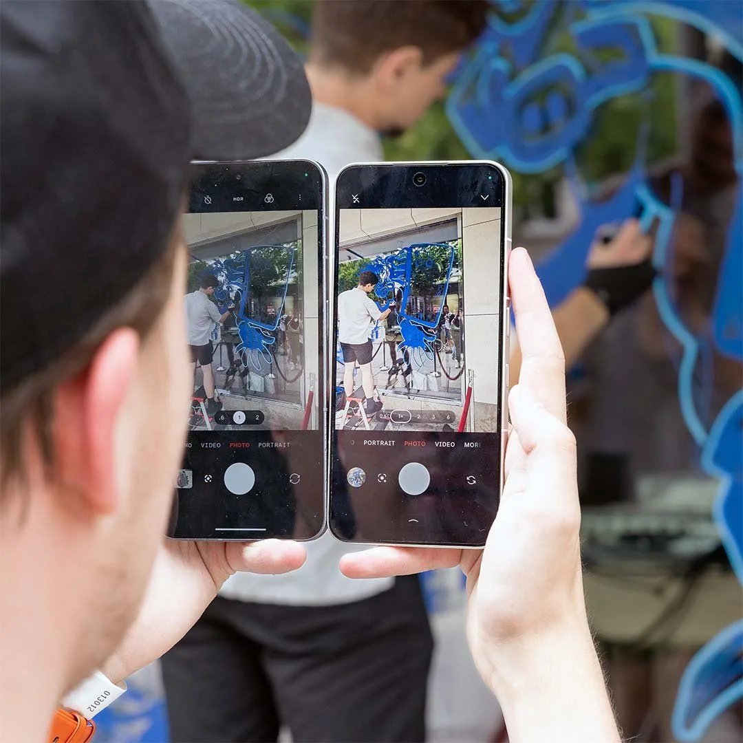 Zwei Menschen fotografieren eine Wand mit blauer Graffiti-Kunst mit ihren Smartphones.
