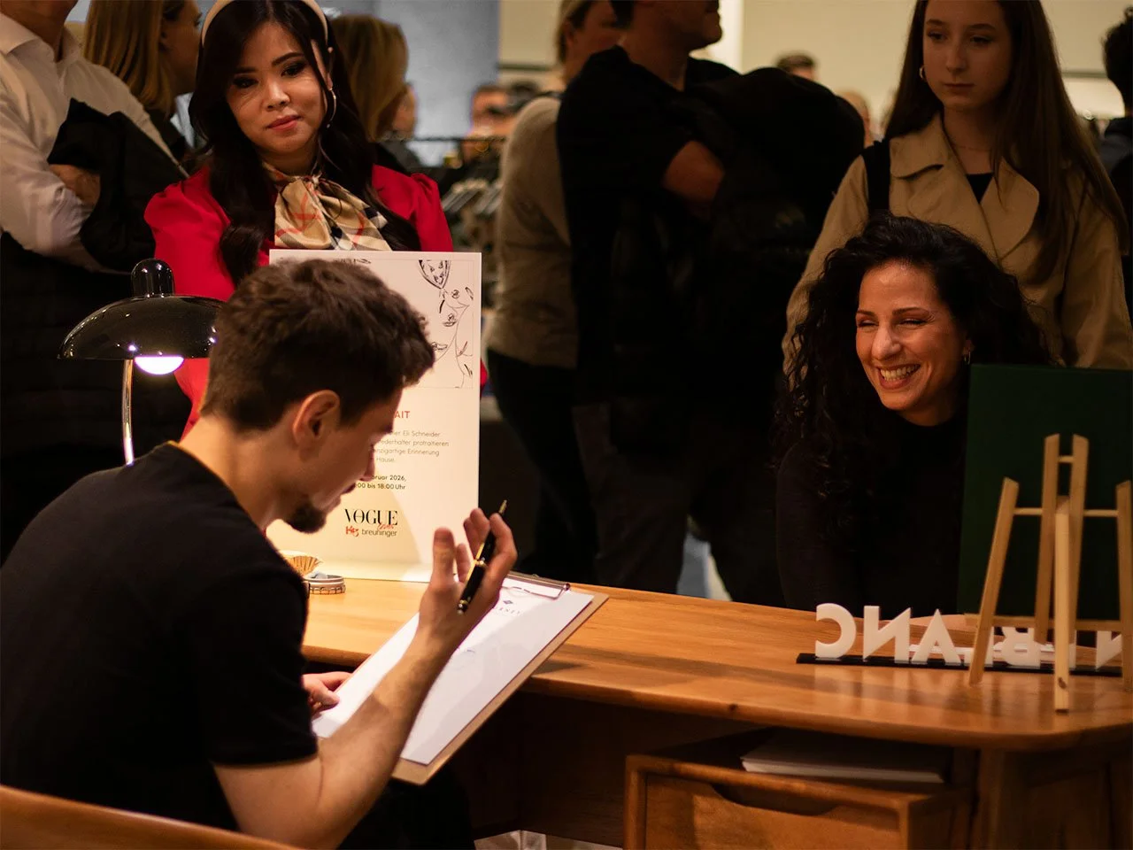 Eine Frau wird von Eli Schneider, Live-Künstler und Event-Illustrator, gezeichnet und lacht dabei. Darum stehen interessierte Beobachter und schauen zu.