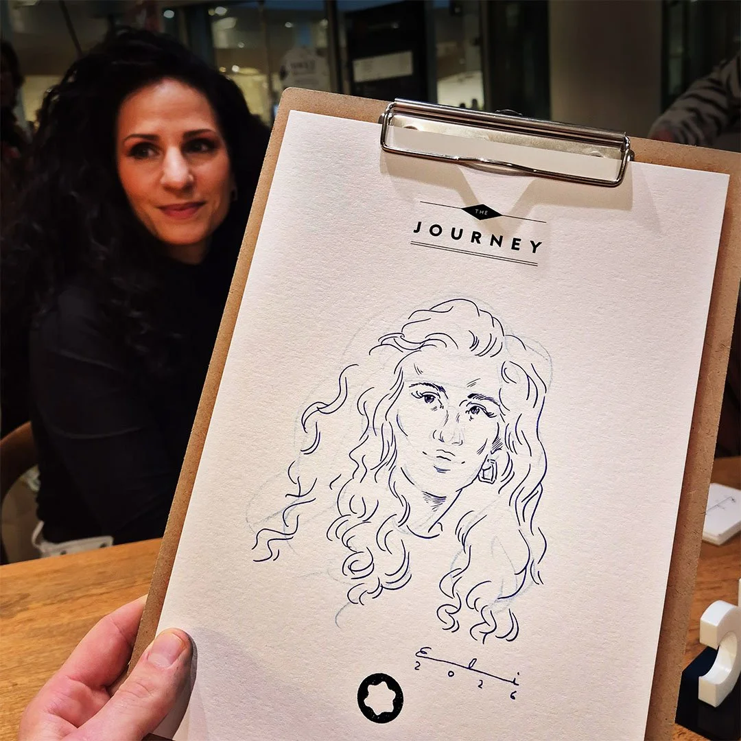 Zeichnung einer Frau mit langen, lockigen Haaren auf einem Klemmbrett; im Hintergrund eine Frau mit dunklen, lockigen Haaren, die auf einen Bildschirm blickt.