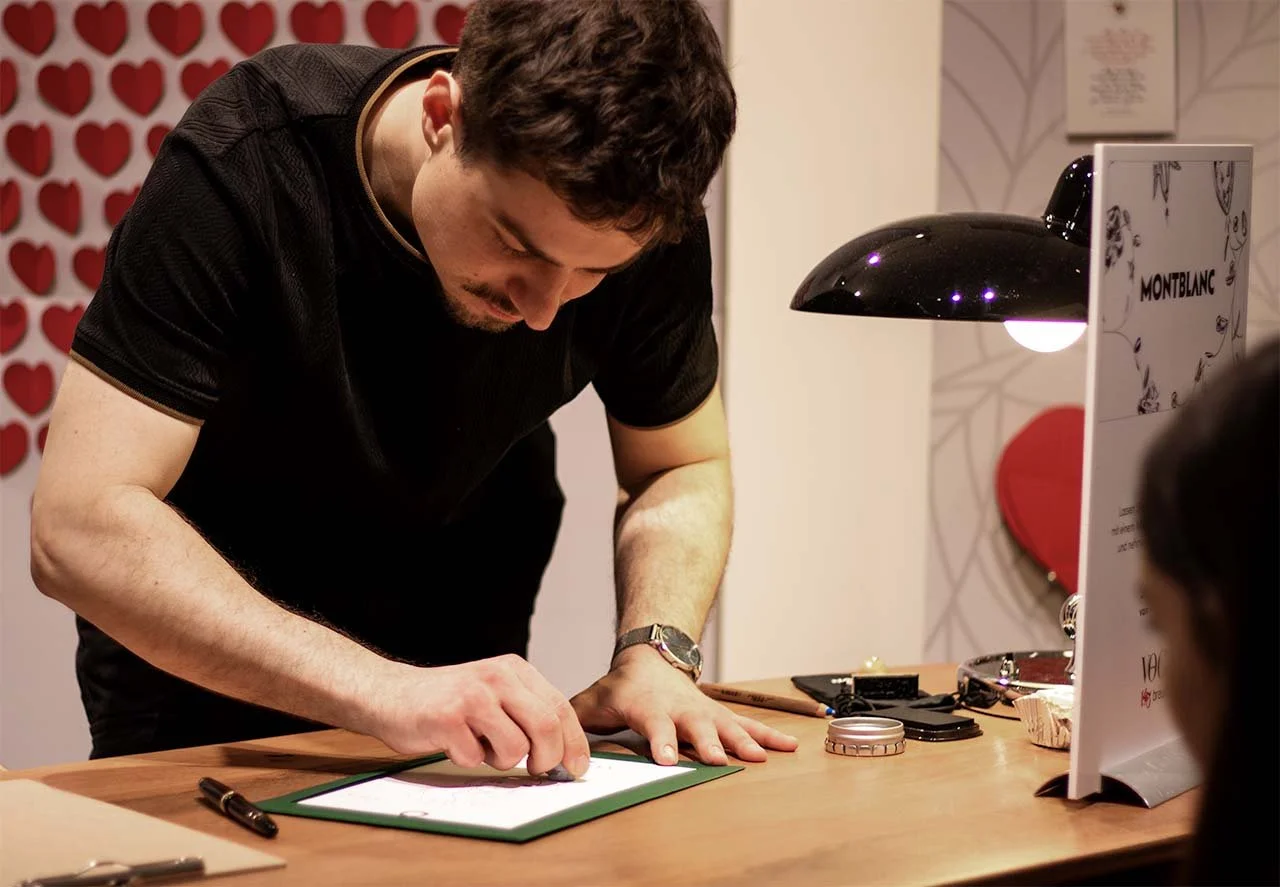 Mann schreibt auf eine Unterschriftsmappe bei einer Veranstaltung in einem Raum mit Herz-Dekoration an der Wand.