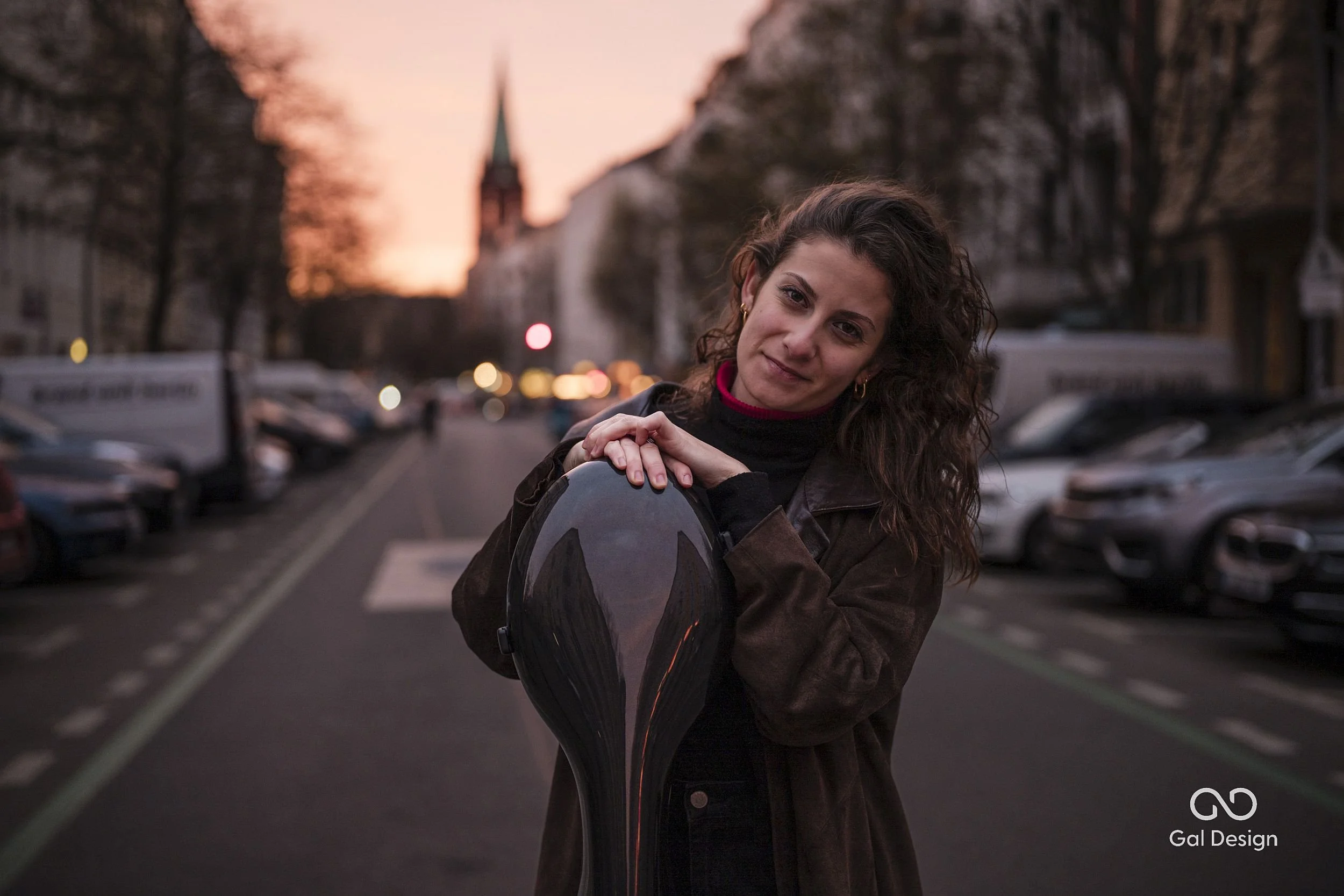 A young woman, standing on the street with a cello case infront of her