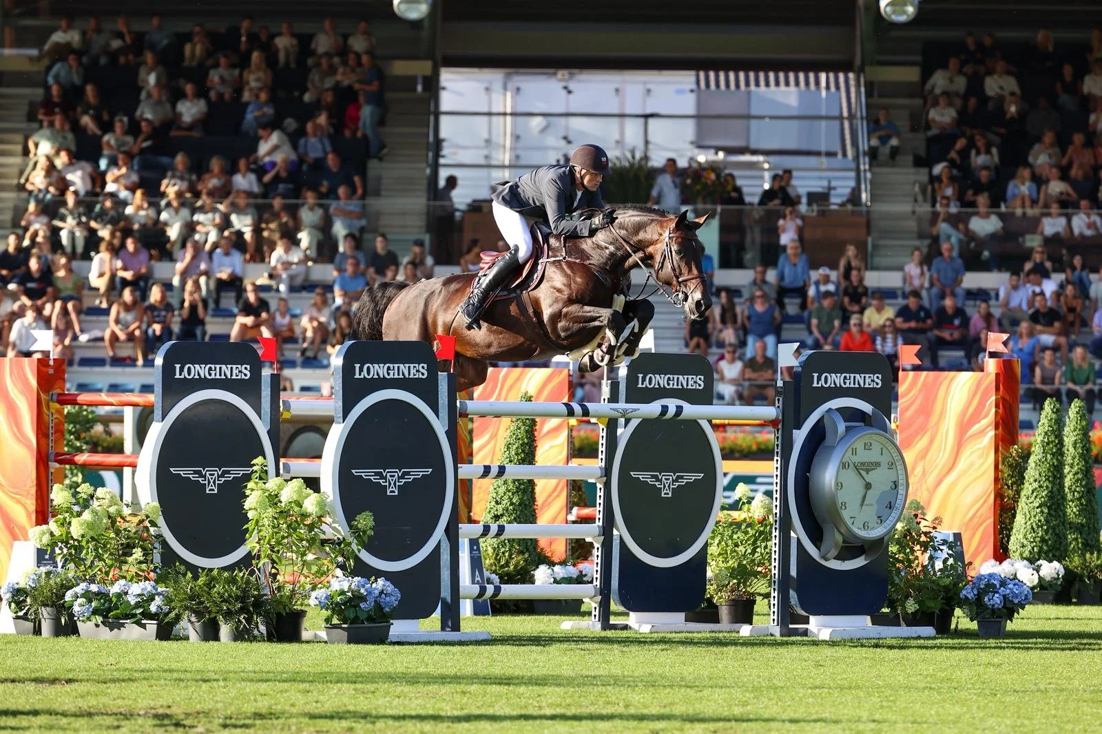 A show jumping equestrian event with a rider guiding a horse over a hurdle. The obstacle has 