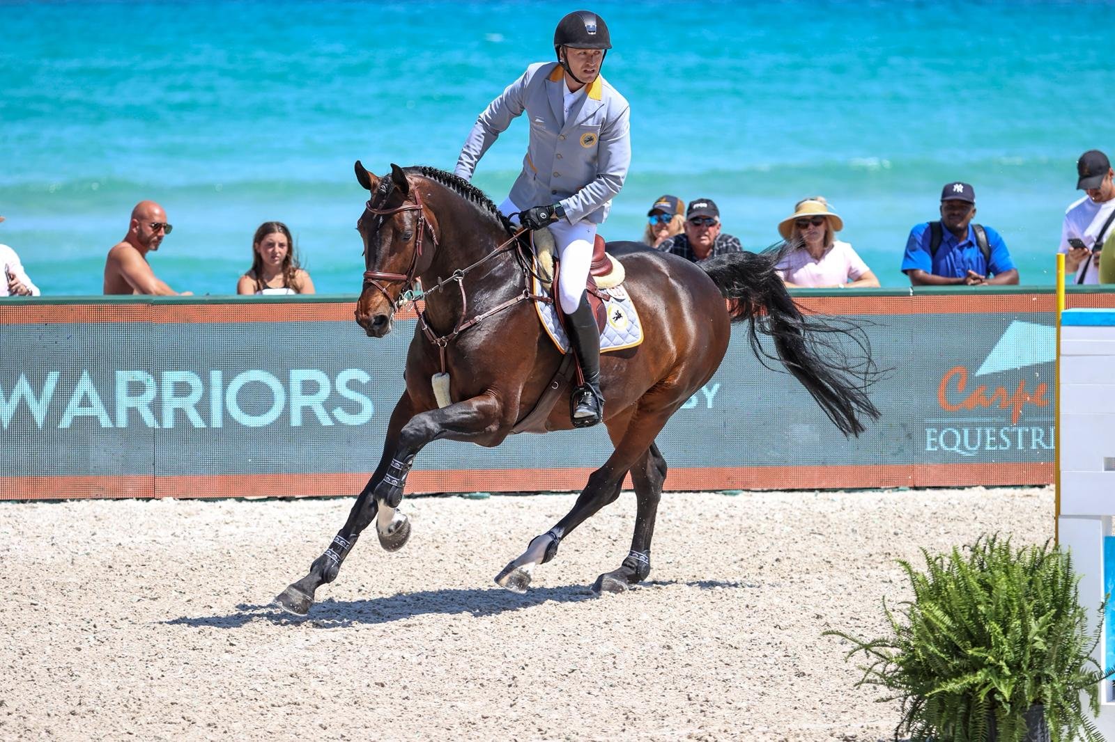 A man riding a horse on a beach during equestrian event with spectators watching from behind a barrier
