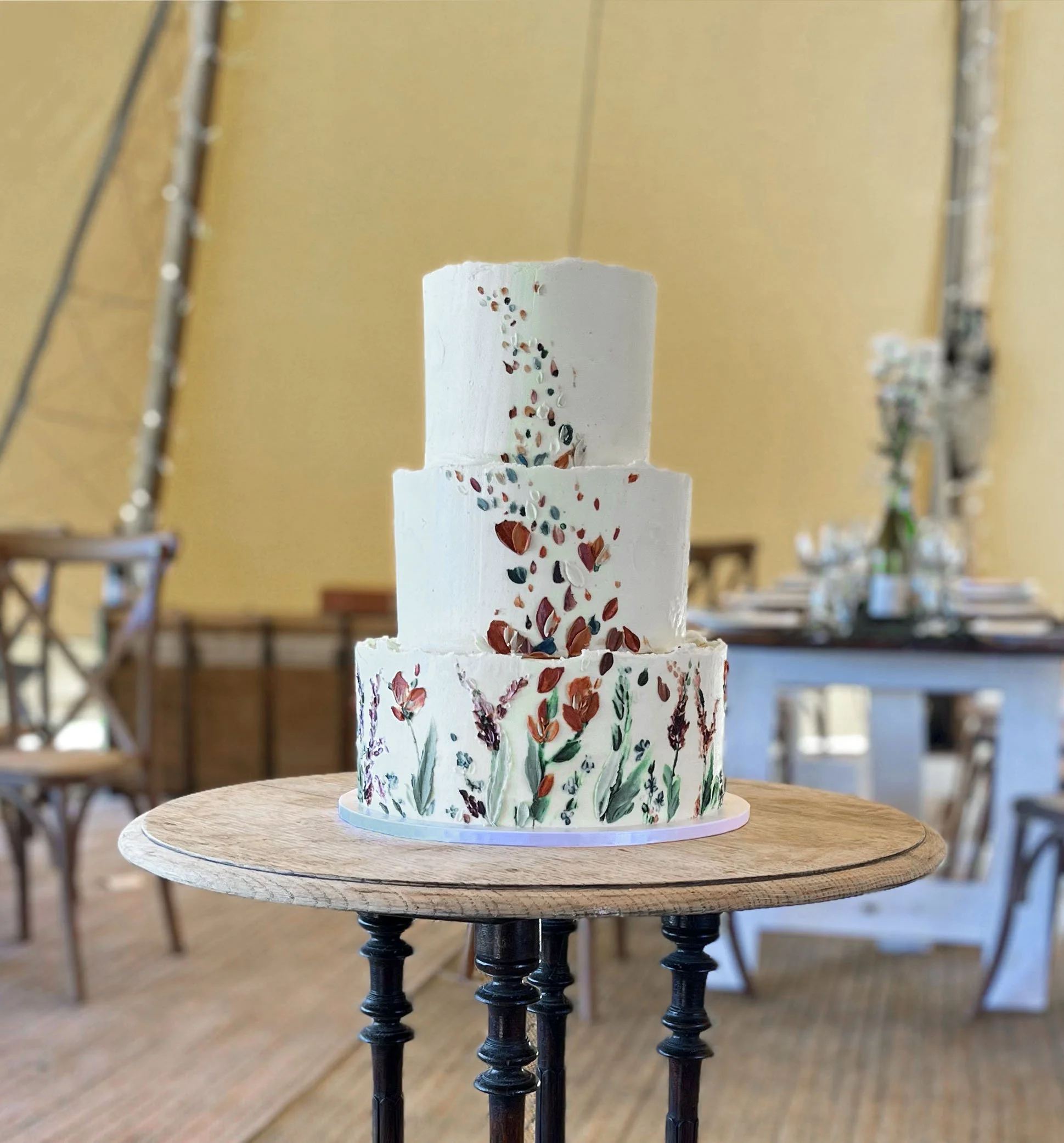 A three-tier vegan wedding cake for an outside wedding with wildflowers and petals snaking up the height of the cake, displayed in Frome, Somerset