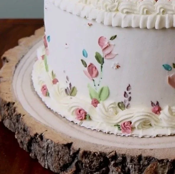 A close up of a vegan birthday cake that has vintage piping and colourful painted flowers in buttercream