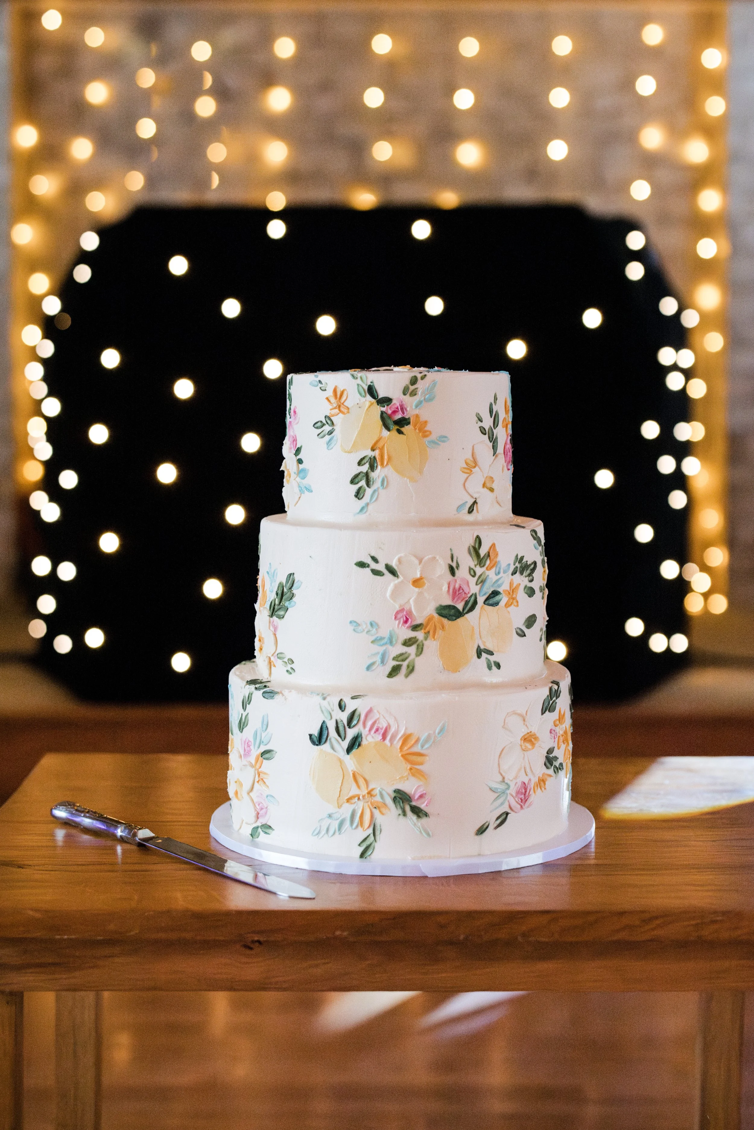 Three tier wedding cake with an Italian theme including lemons, olive leaves and pale blue flowers displayed in Wiltshire