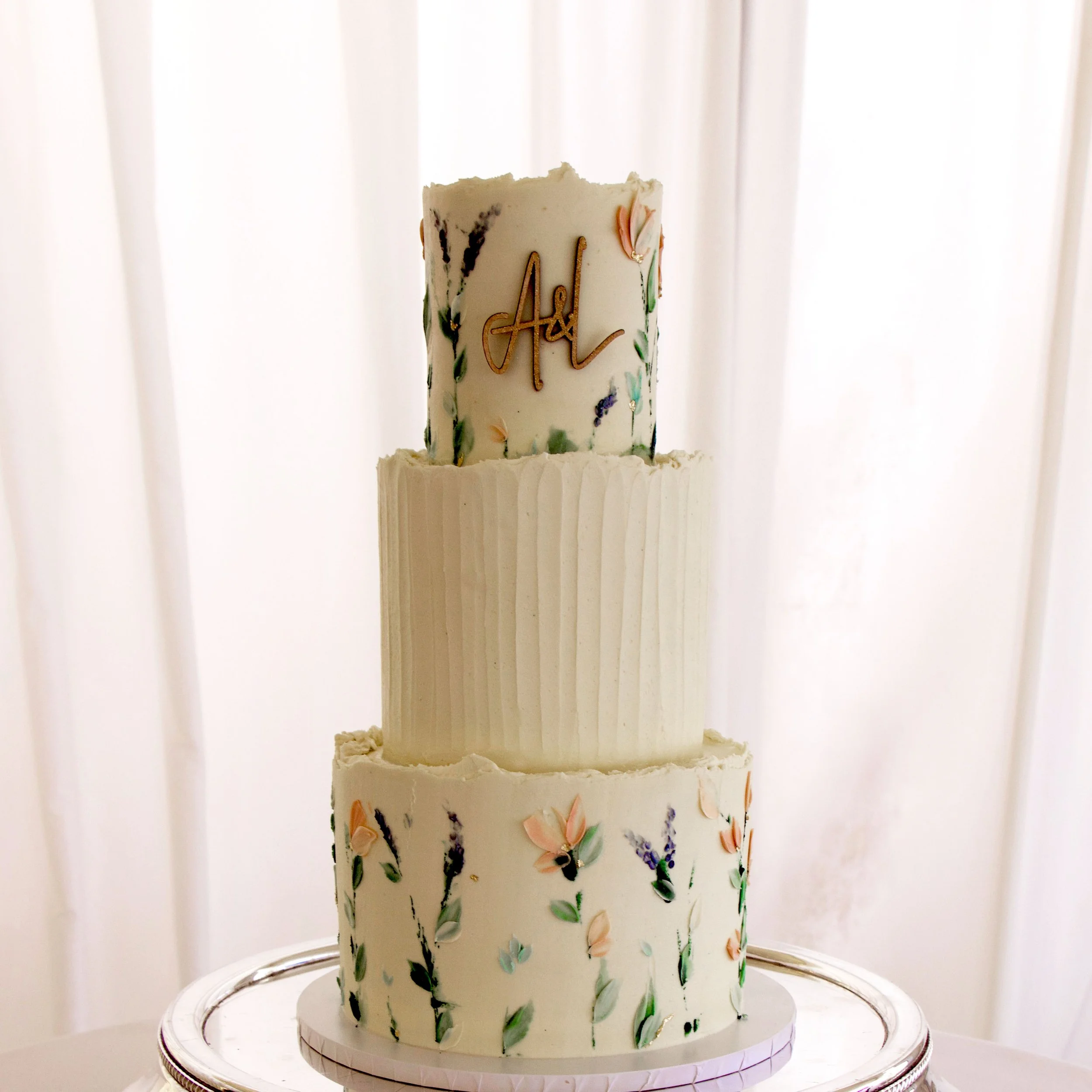 A three tier bespoke vegan wedding cake with wildflowers and the couples initials in wood on the front