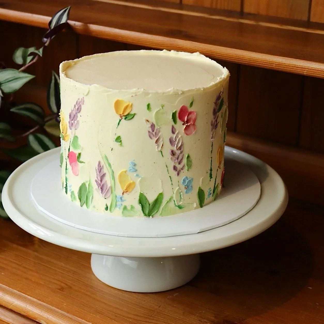 cream coloured celebration cake on a white cake stand with a meadow theme