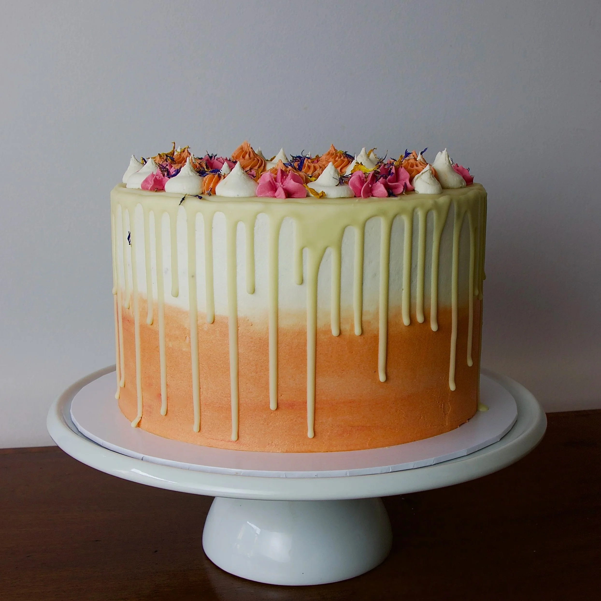 a white and coral celebration cake with white chocolate drips, piping and edible petals