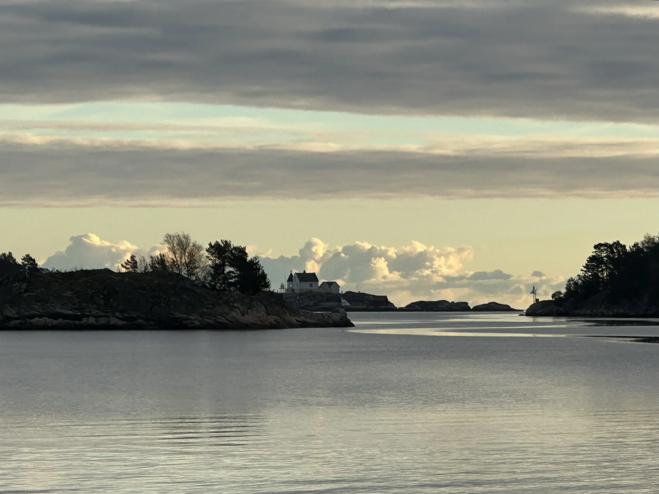 Scenic view of rocky coastline with trees, a white church, and water under a cloudy sky.