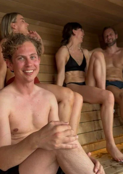 En gruppe mennesker smiler og ler inne i en badstue