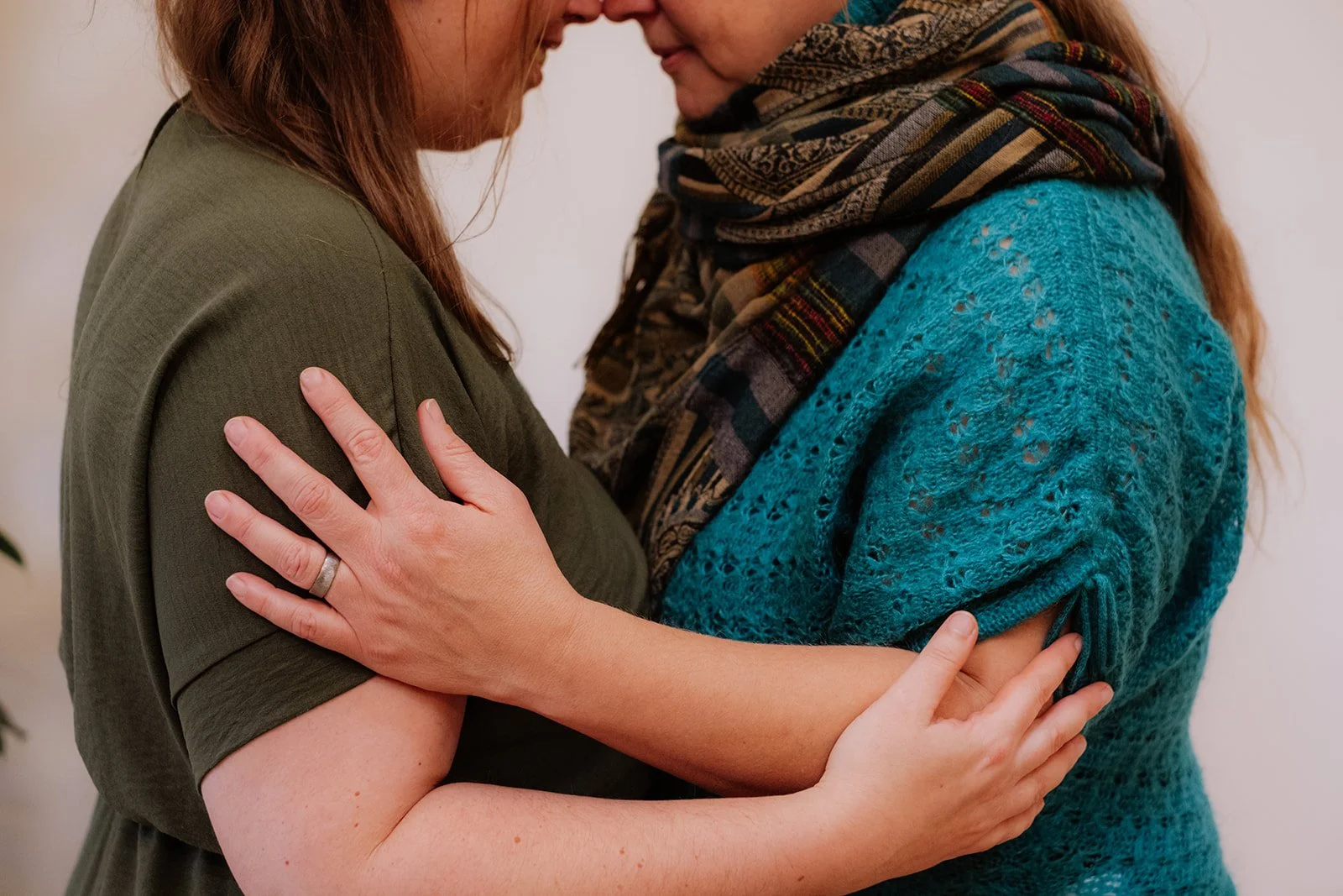 Twee vrouwen houden elkaar dicht vast in een omhelzing, voorhoofd tegen voorhoofd, met handen op elkaars schouders en armen.