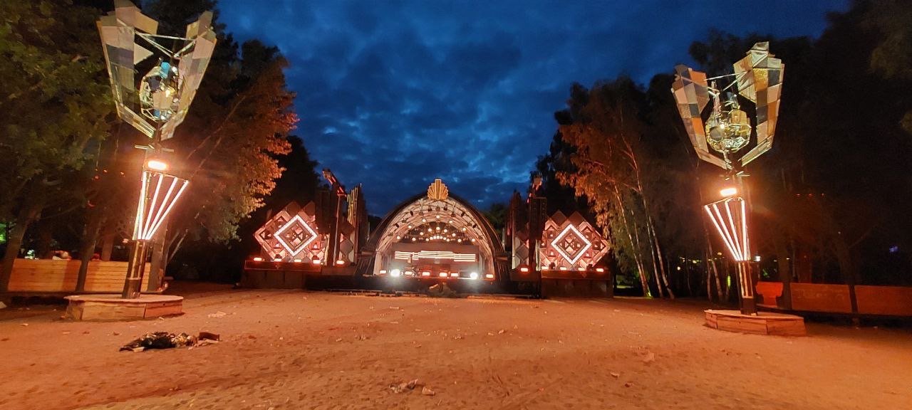 Leerer Tanzfläche mit bunten, futuristischen Skulpturen und Gebäuden, bei Nacht mit dunklem Himmel.