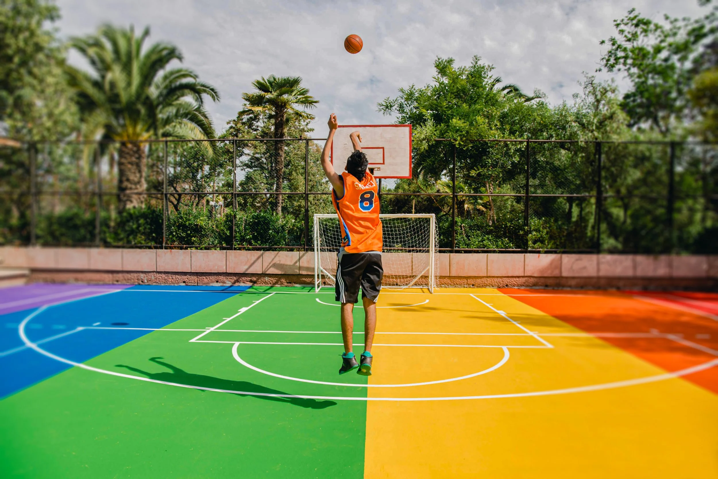 Joven jugando baloncesto en una cancha de colores vibrantes, lanzando una pelota hacia la cesta mientras hace un tiro libre.
