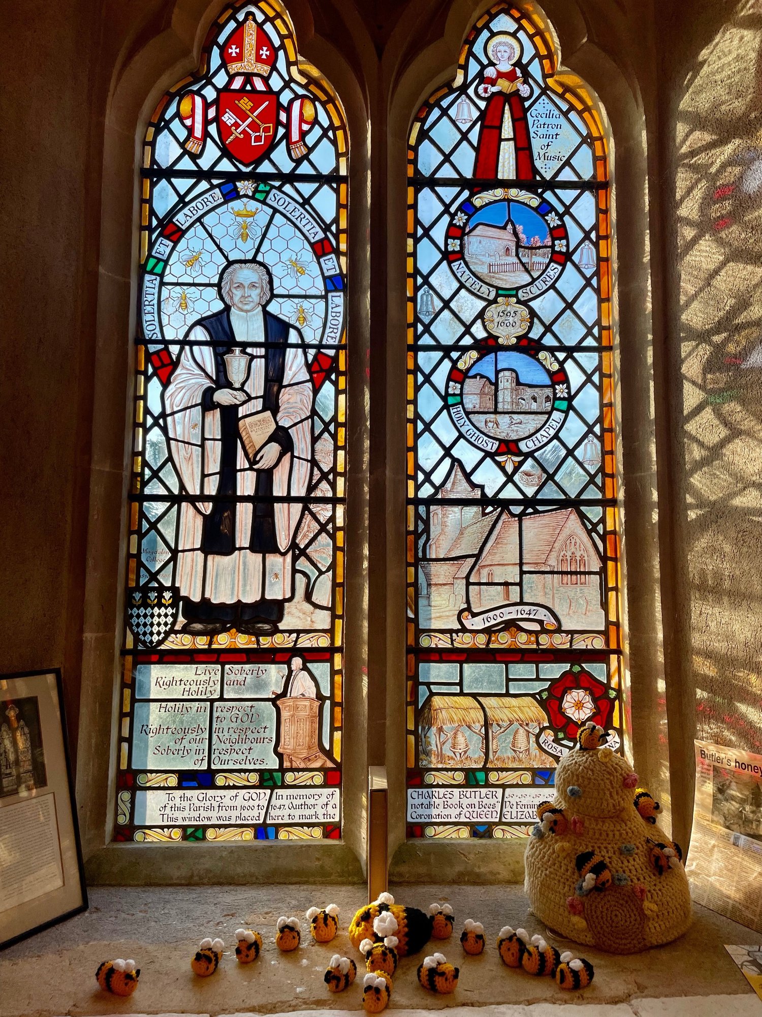 The Charles Butler stained glass window, two panels with Latin inscriptions and scenes from his life, with a crocheted bee on the windowsill