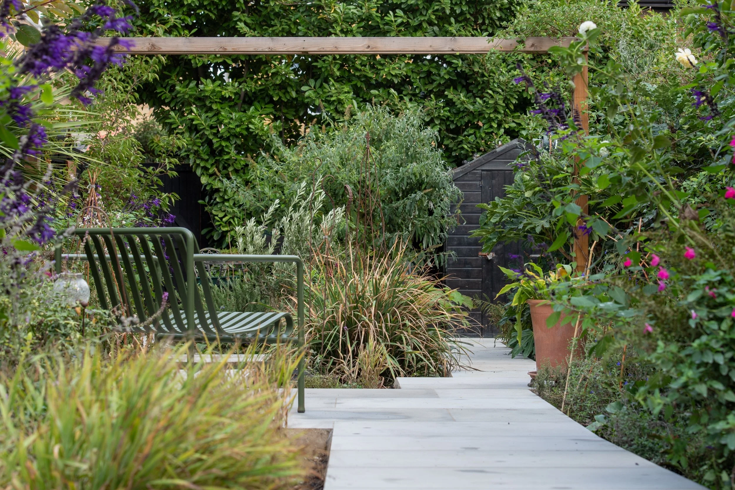 View through a timber pergola and lush planting to the house and paved terrace in a Wimbledon back garden by Vlad the Landscaper