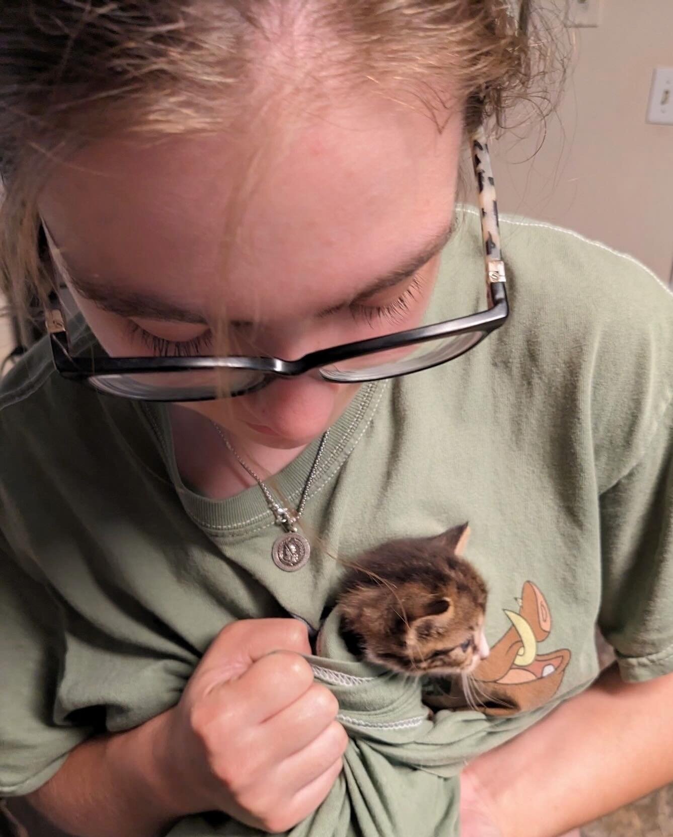 Mollie holds a small, neonatal kitten with brown, black, and white fur close to her chest.