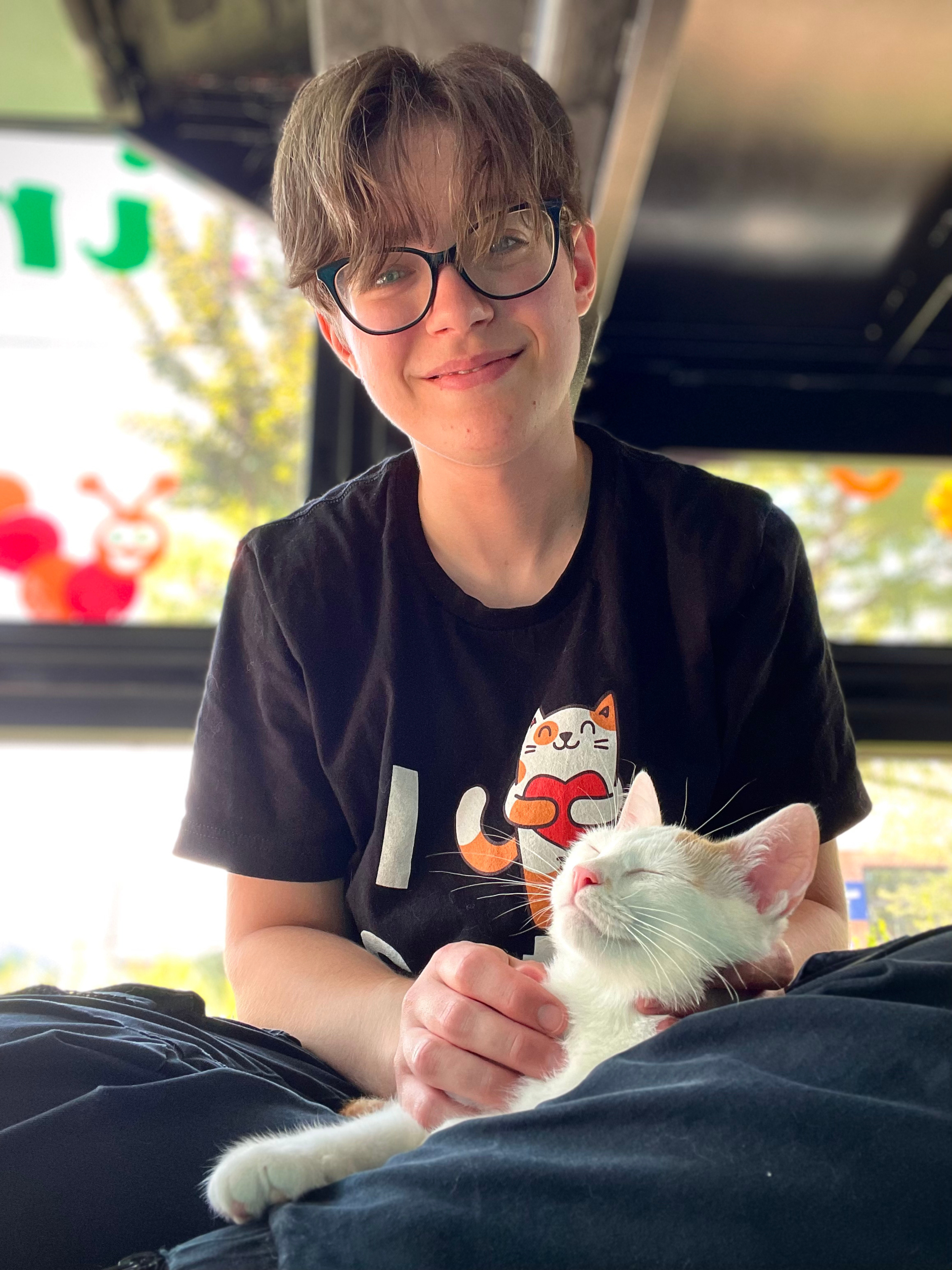 A picture of Mollie Joyner, the founder and main cat-sitter for Kissies For Your Hissies. In this picture, she is sitting with a cat looking blissfully asleep in her lap