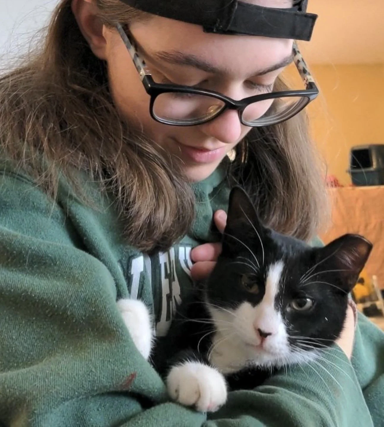 Mollie Joyner wearing a green sweatshirt holding a black and white cat with a TNVR ear clip close to her chest.
