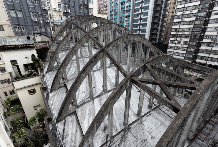 A rooftop with multiple curved, arching concrete beams, surrounded by high-rise buildings in an urban area.
