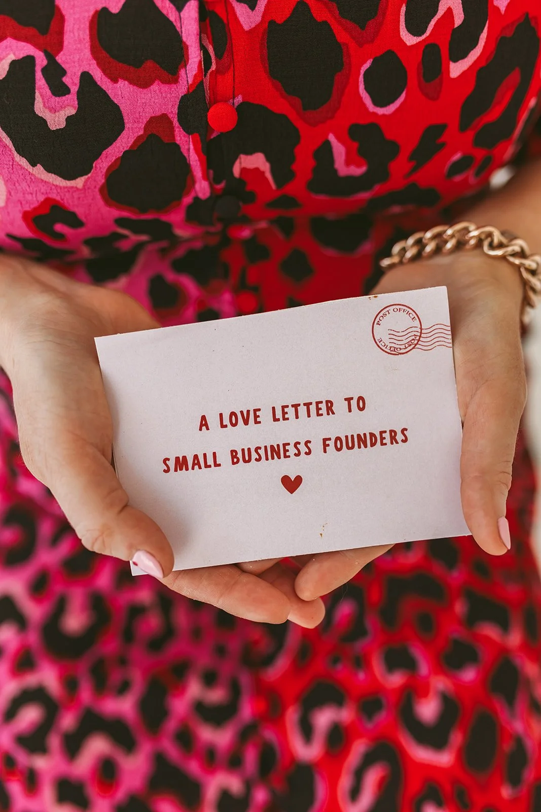 Person holding an envelope with the text 'A love letter to small business founders' in red, wearing a colorful patterned dress.