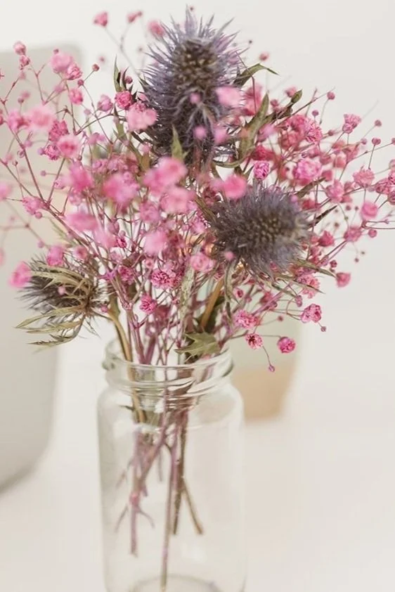 A bouquet of pink baby's breath flowers with purple thistle, arranged in a clear glass jar.