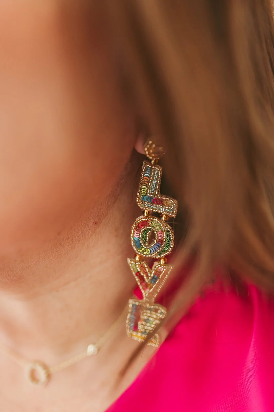 Close-up of a woman's ear wearing large colorful beaded earrings spelling 'LOVE'.