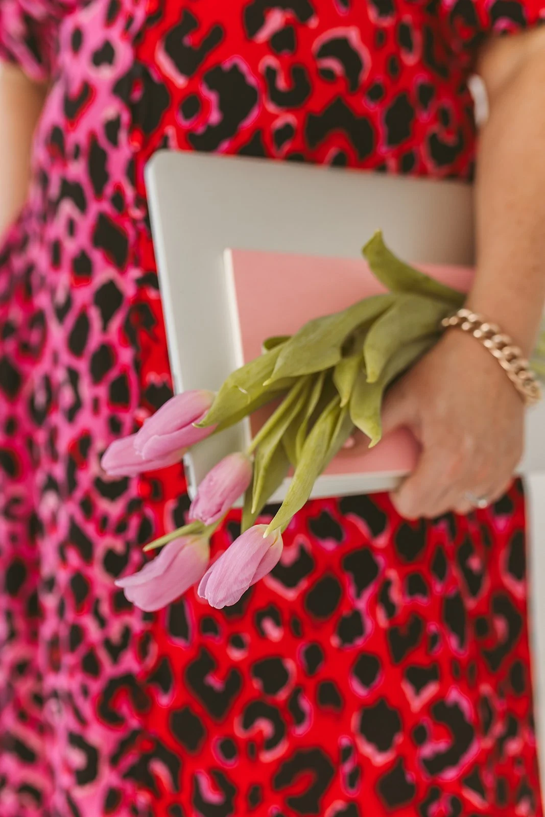 Person holding pink tulips and a laptop against a red and black patterned dress.