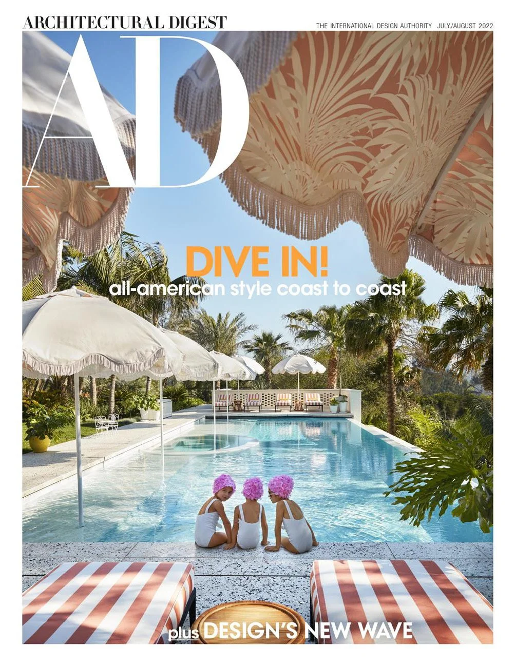 Architectural Digest July/August 2022 cover featuring a poolside view with striped loungers and children in vintage-style swim caps seated at the edge of a turquoise pool