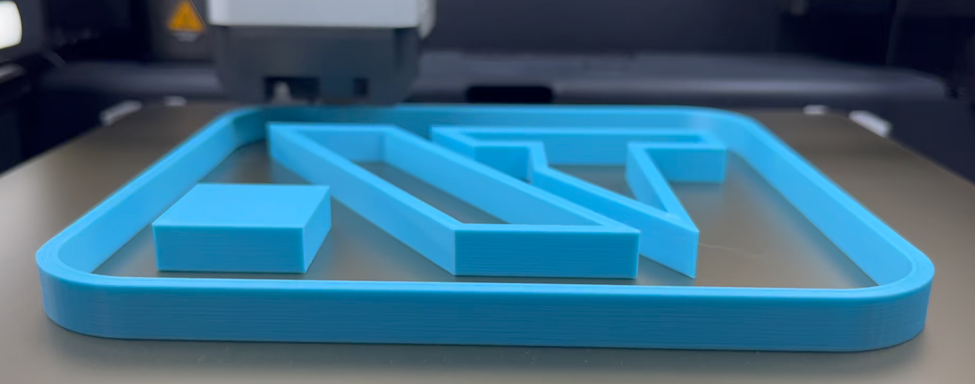 Das Bild zeigt das Navkotec-Logo in hellblauer Schrift auf einem Druckbett in hoher Qualität. Es ist mit dem FDM-Druckverfahren gedruckt.