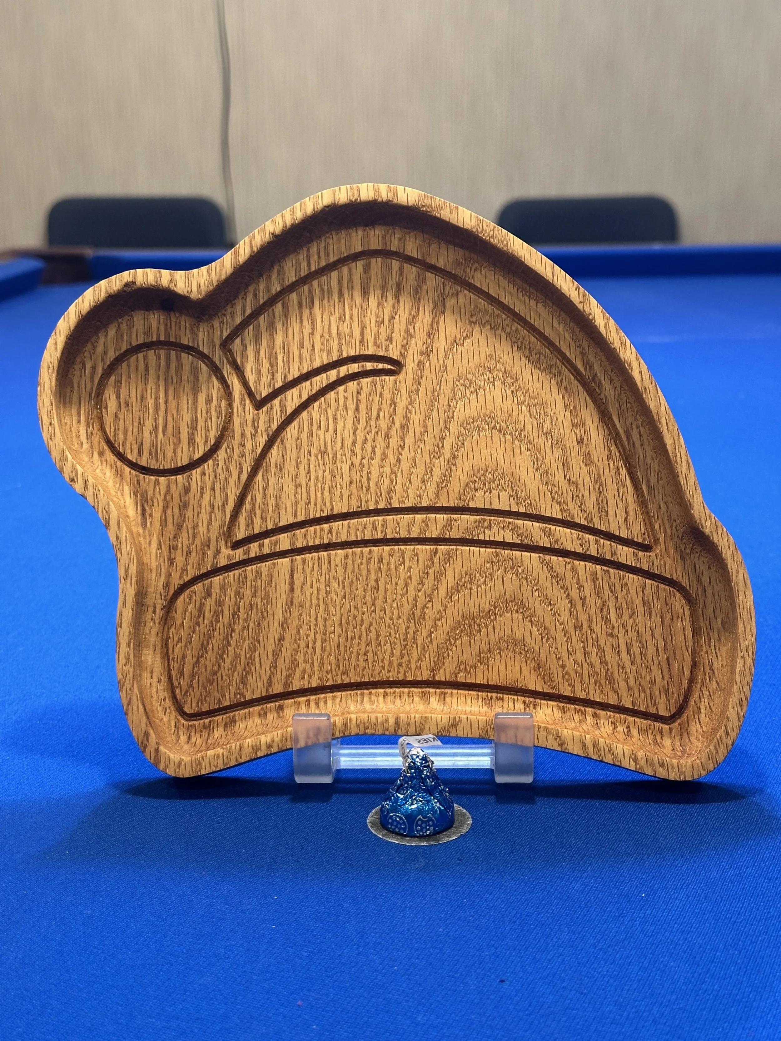 A wooden box with carved patterns featuring a moon and waves, placed on a blue surface with a small wrapped candy in front.