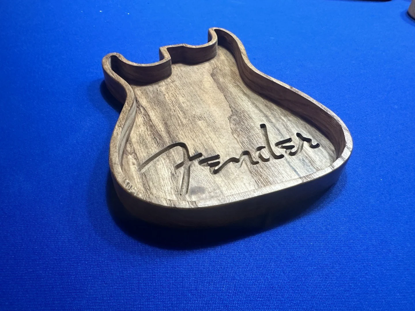 A wooden tray carved in the shape of a guitar with the word 'Fender' engraved inside.