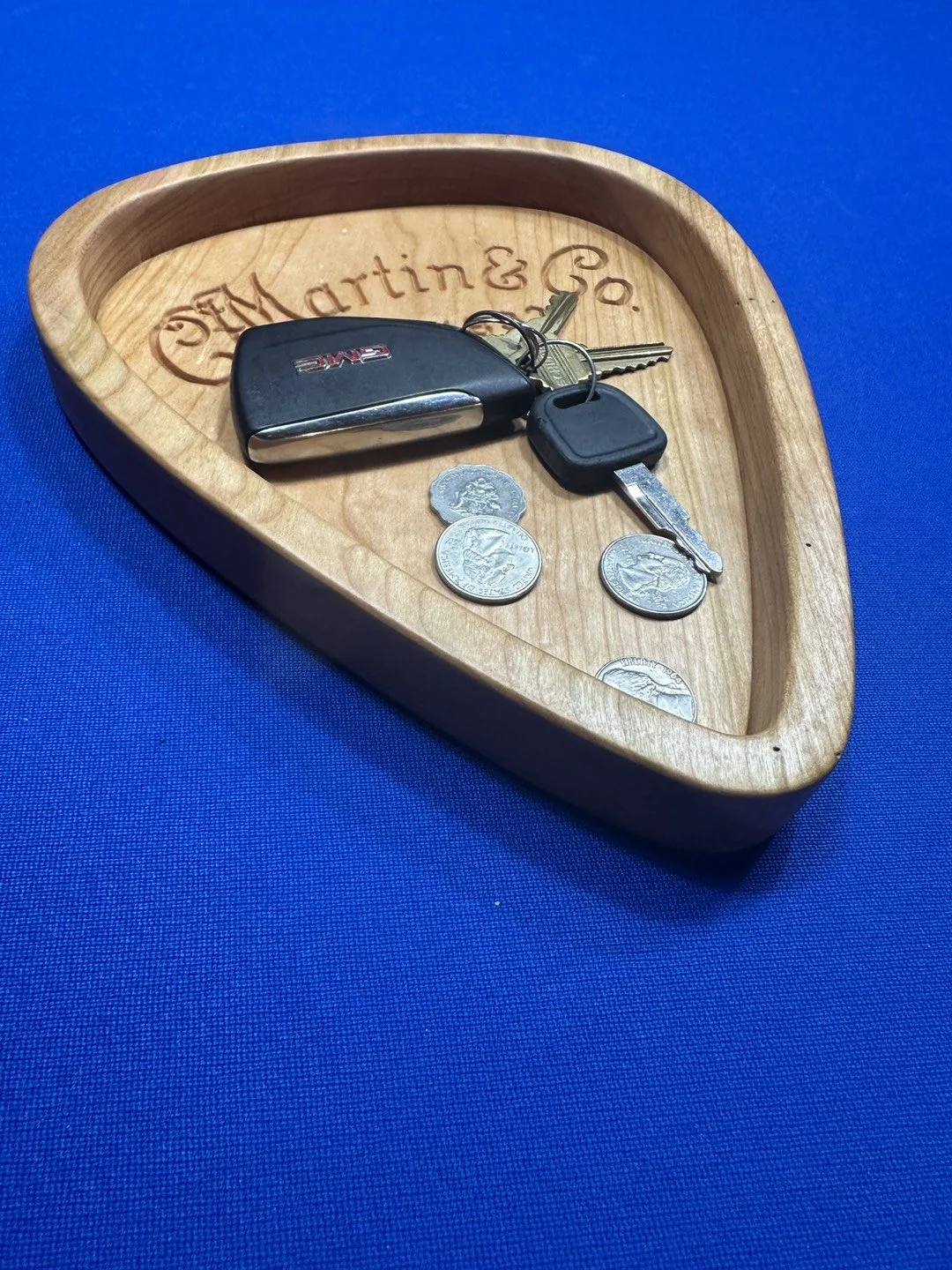 A wooden bowl with the words Martin & Co engraved inside, holding car keys and coins on a blue background.