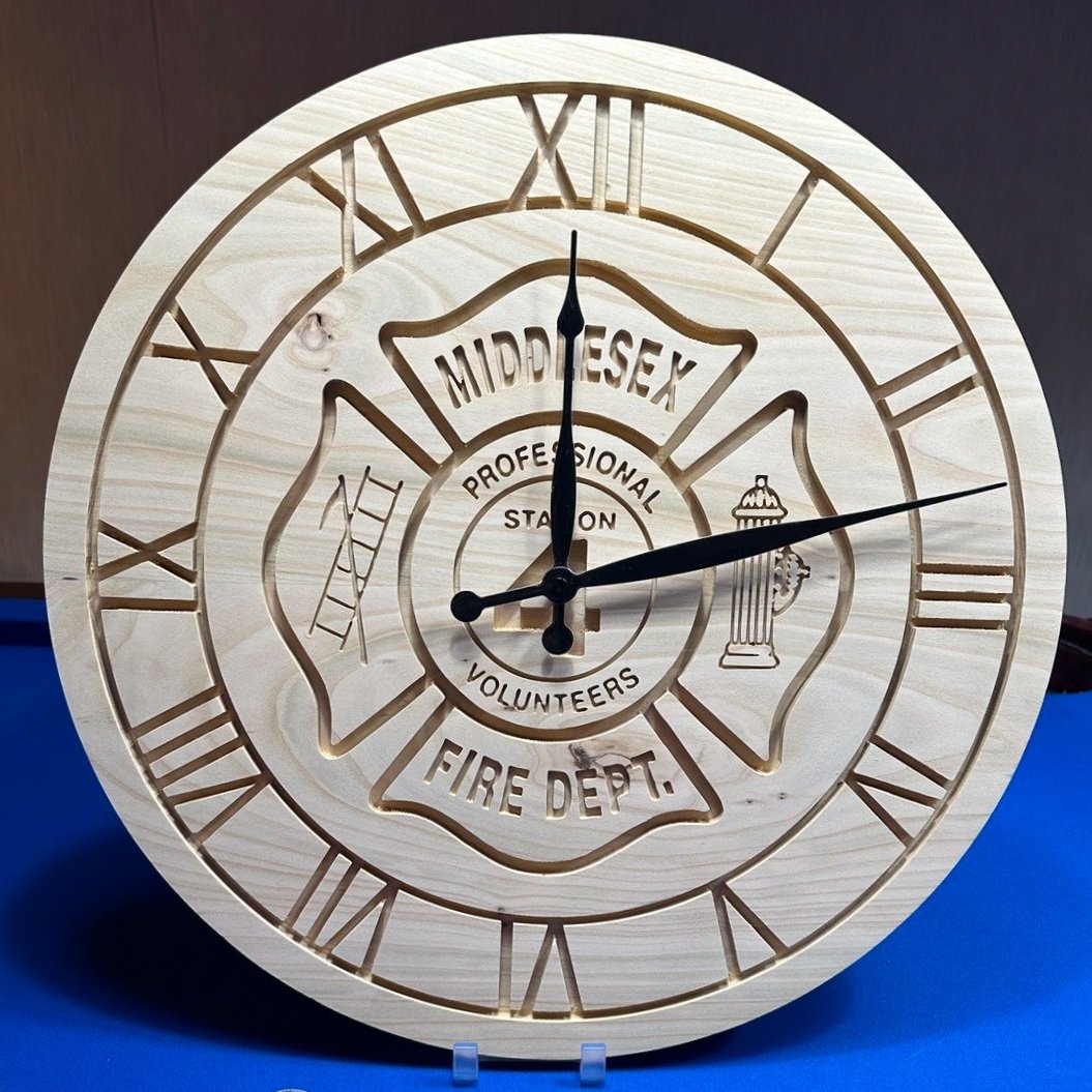 A wooden clock featuring a firefighter emblem with the words 'Middlesex Fire Dept.' and images of a ladder and a fire hydrant, with Roman numerals around the clock face.