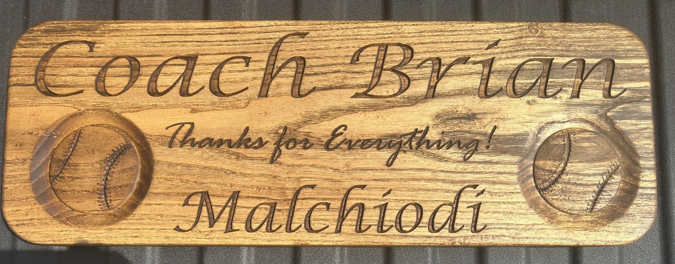 Wooden sign with engraved text reading 'Coach Brian' and 'Machiodi,' featuring two engraved baseballs, and the message 'Thanks for Everything!'