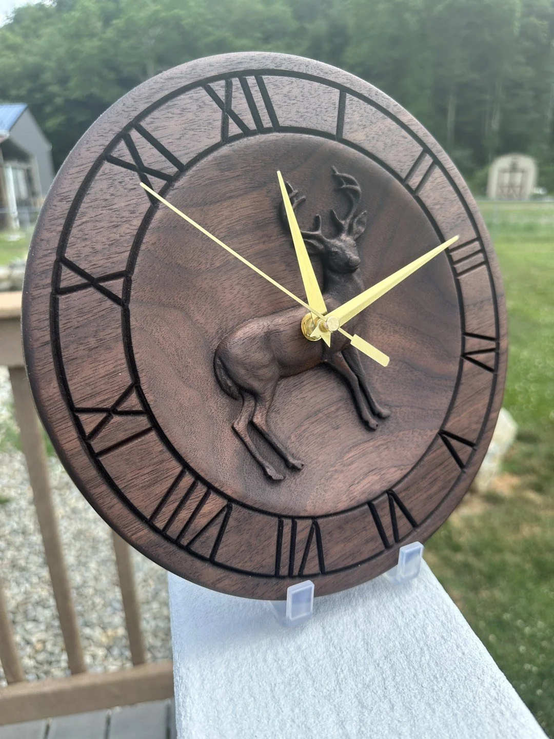 Wooden wall clock with Roman numerals and a 3D carved deer in the center; gold-colored hour and minute hands, and a thin second hand.
