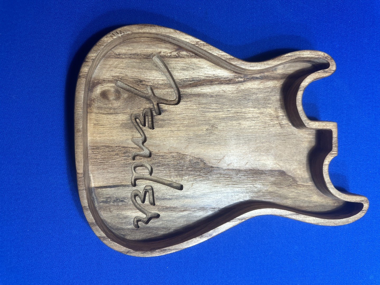 Wooden serving tray in the shape of Texas with the word "Texas" engraved on it, placed on a blue surface.