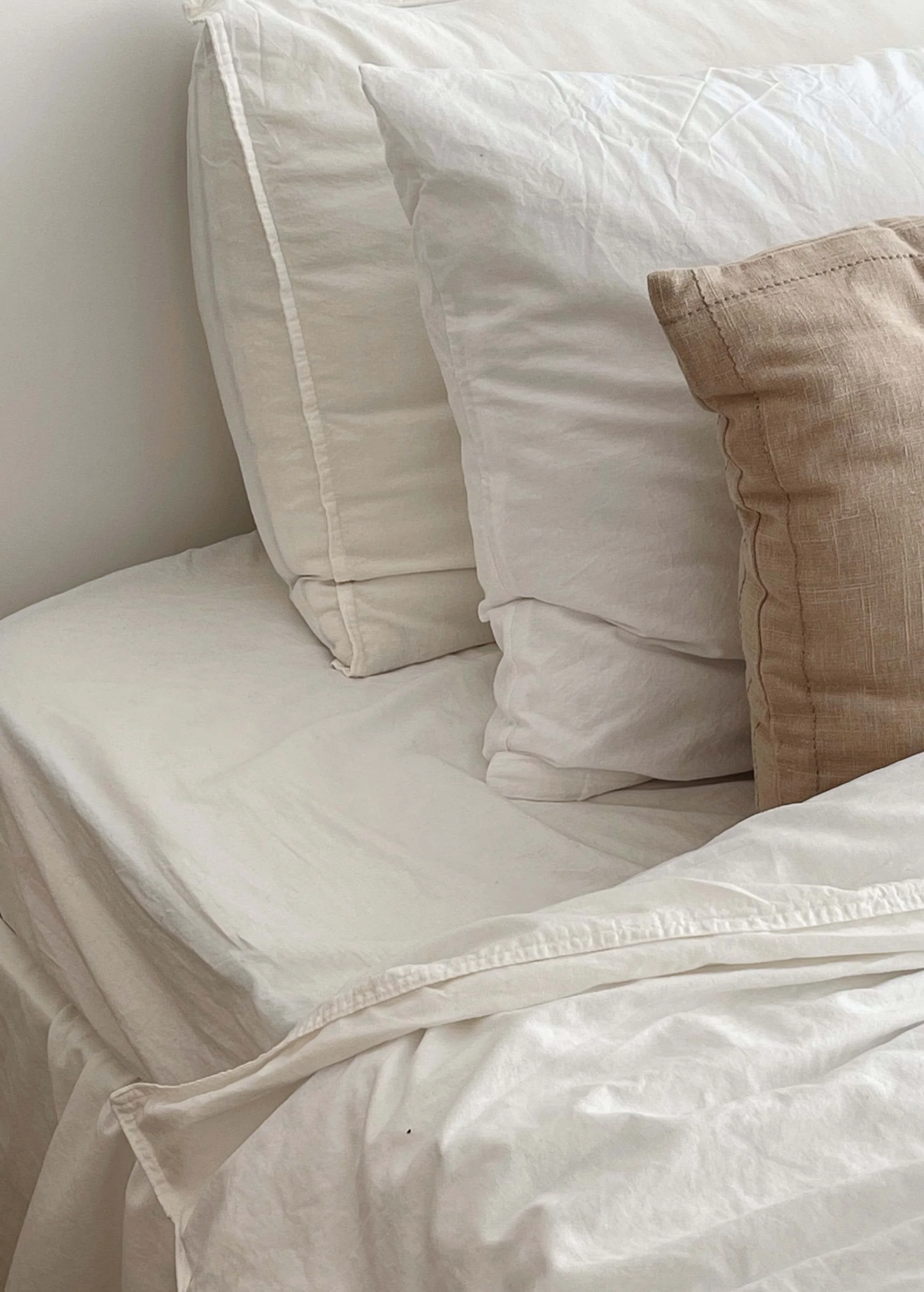 A neatly made bed with white sheets, large white pillows, and a smaller beige pillow on top.