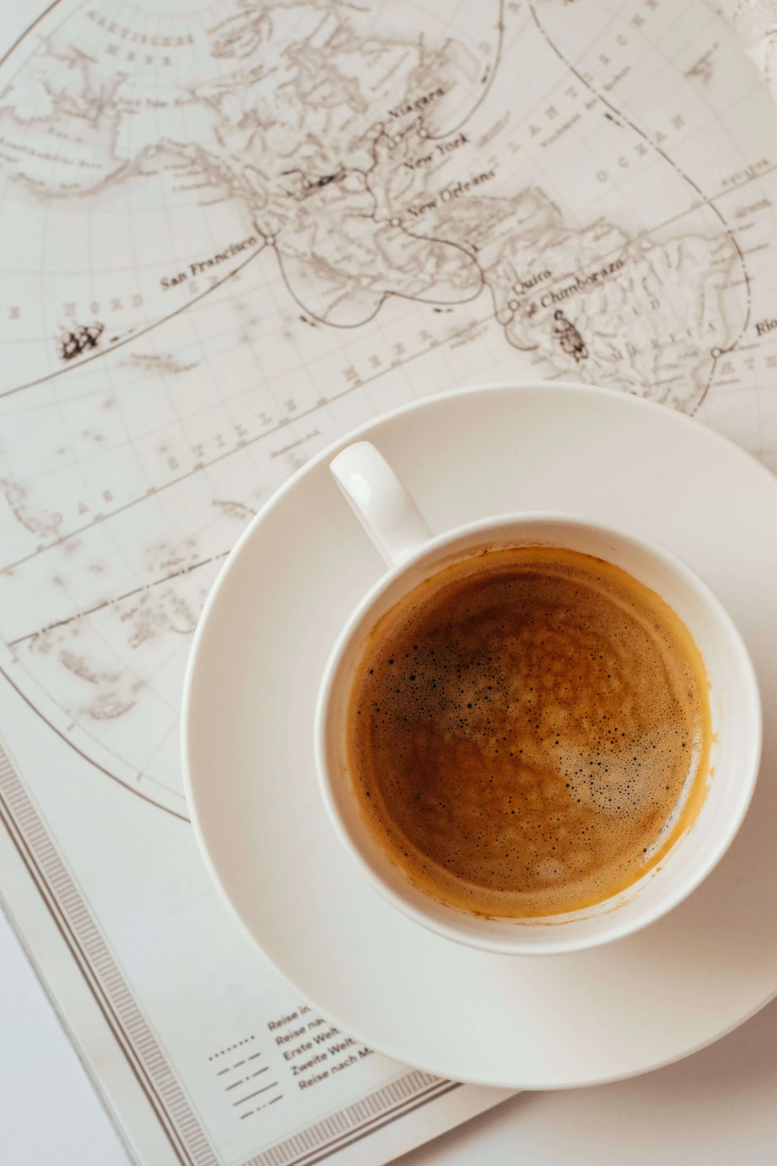 A white cup of coffee placed on a saucer on top of a world map, with the map showing parts of North America and Central America.