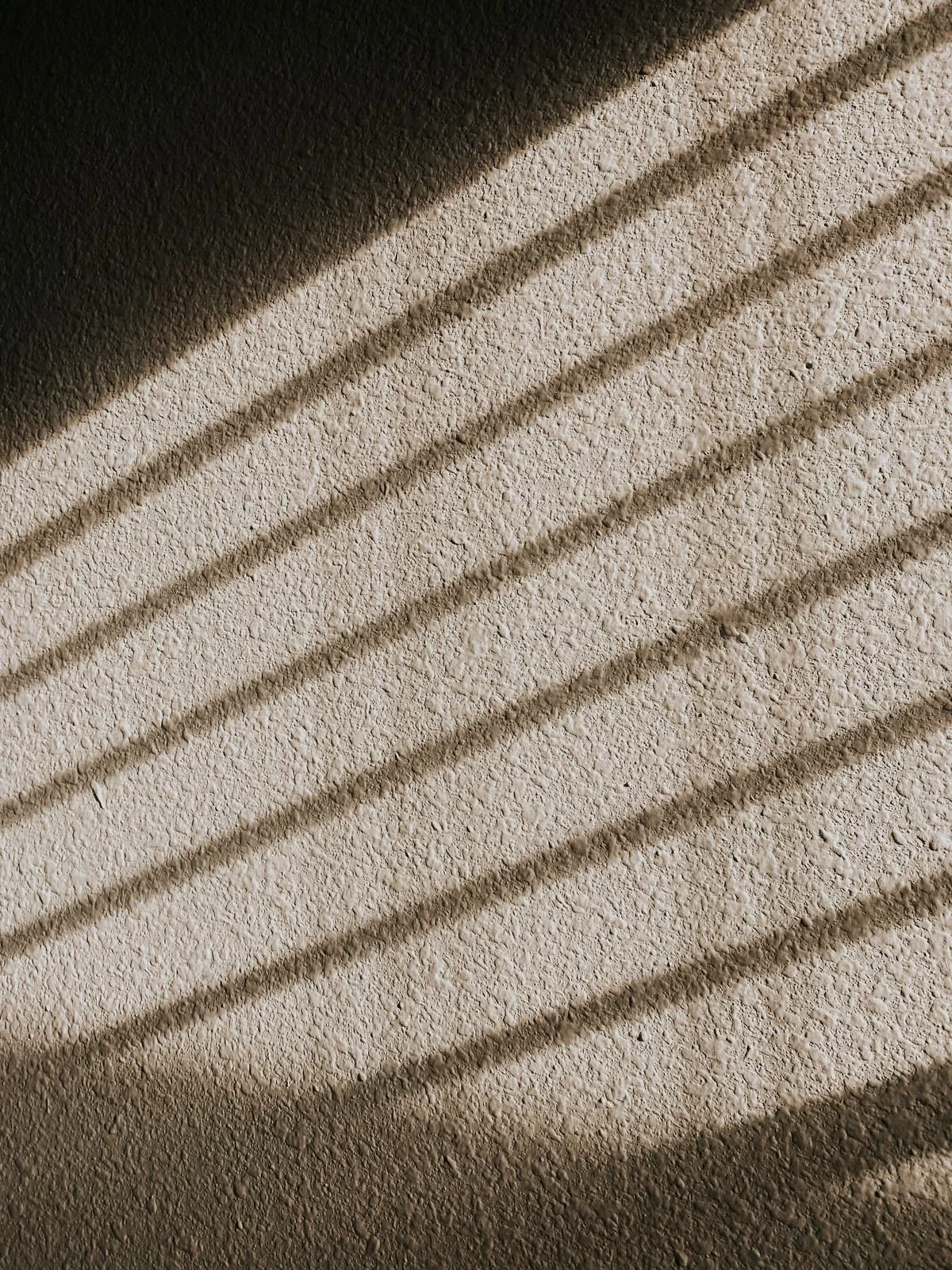 Close-up of textured wall with diagonal shadows cast across it.