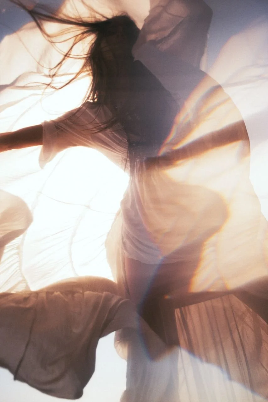 Woman sitting on a translucent fabric under sunlight, with rainbow effects caused by light refraction.