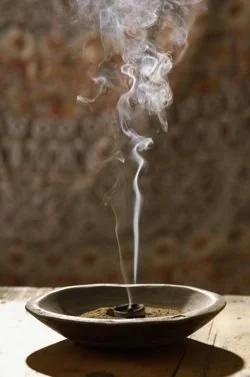 A burning incense stick emitting smoke over a small dish