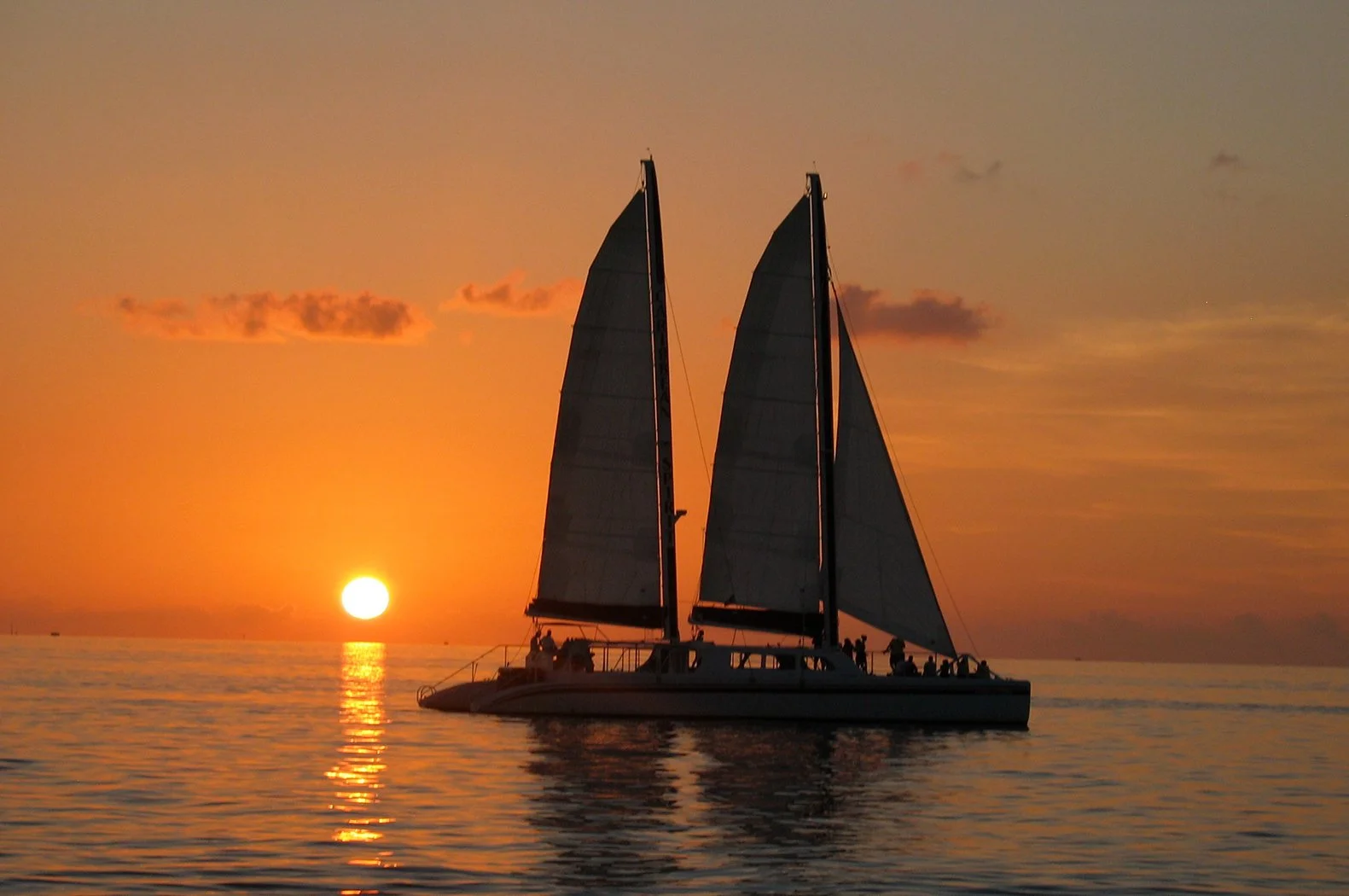 Sailboat on calm water at sunset with orange sky and reflection