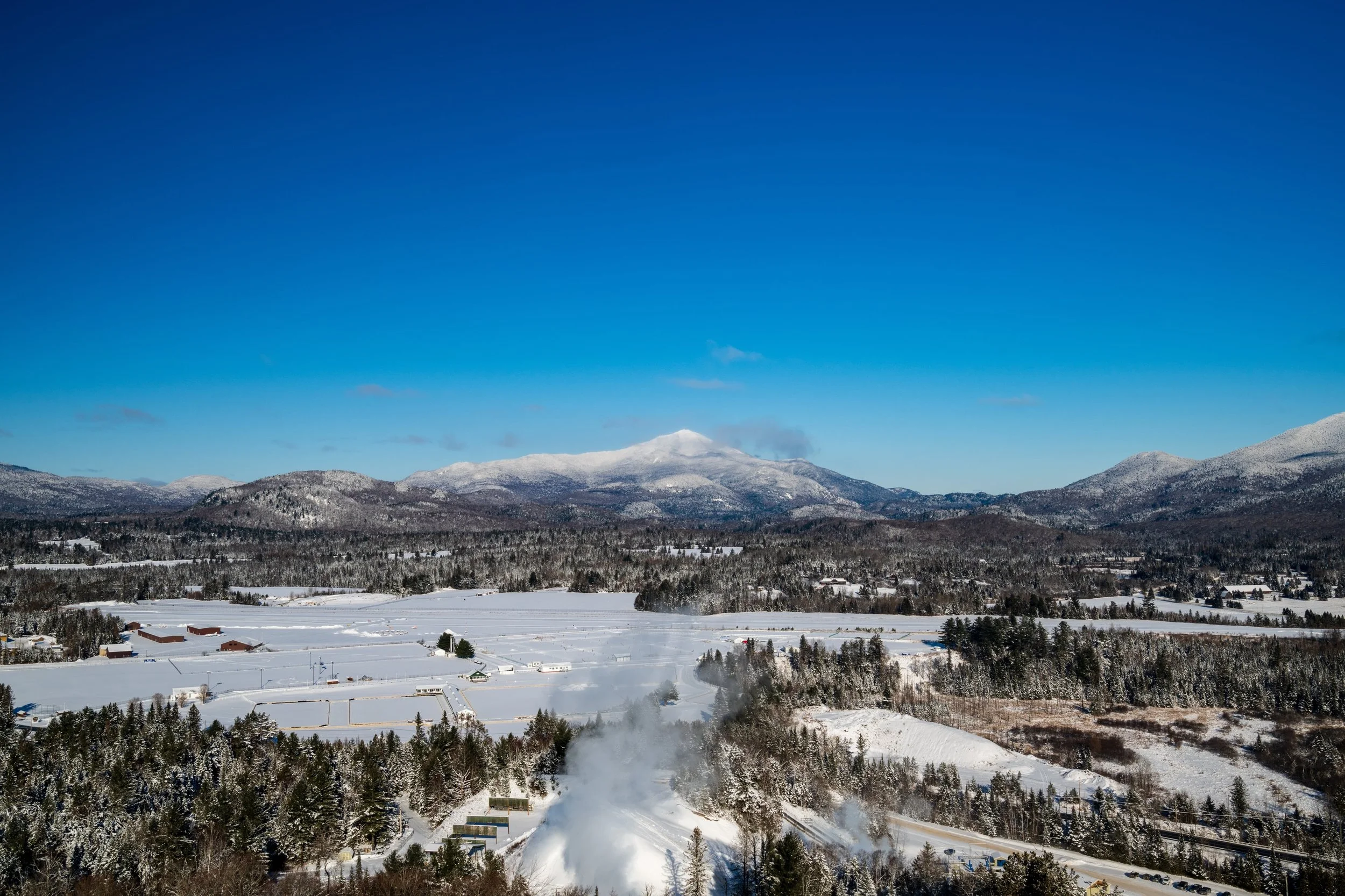 Snow-covered landscape with mountains in the background under a clear blue sky.