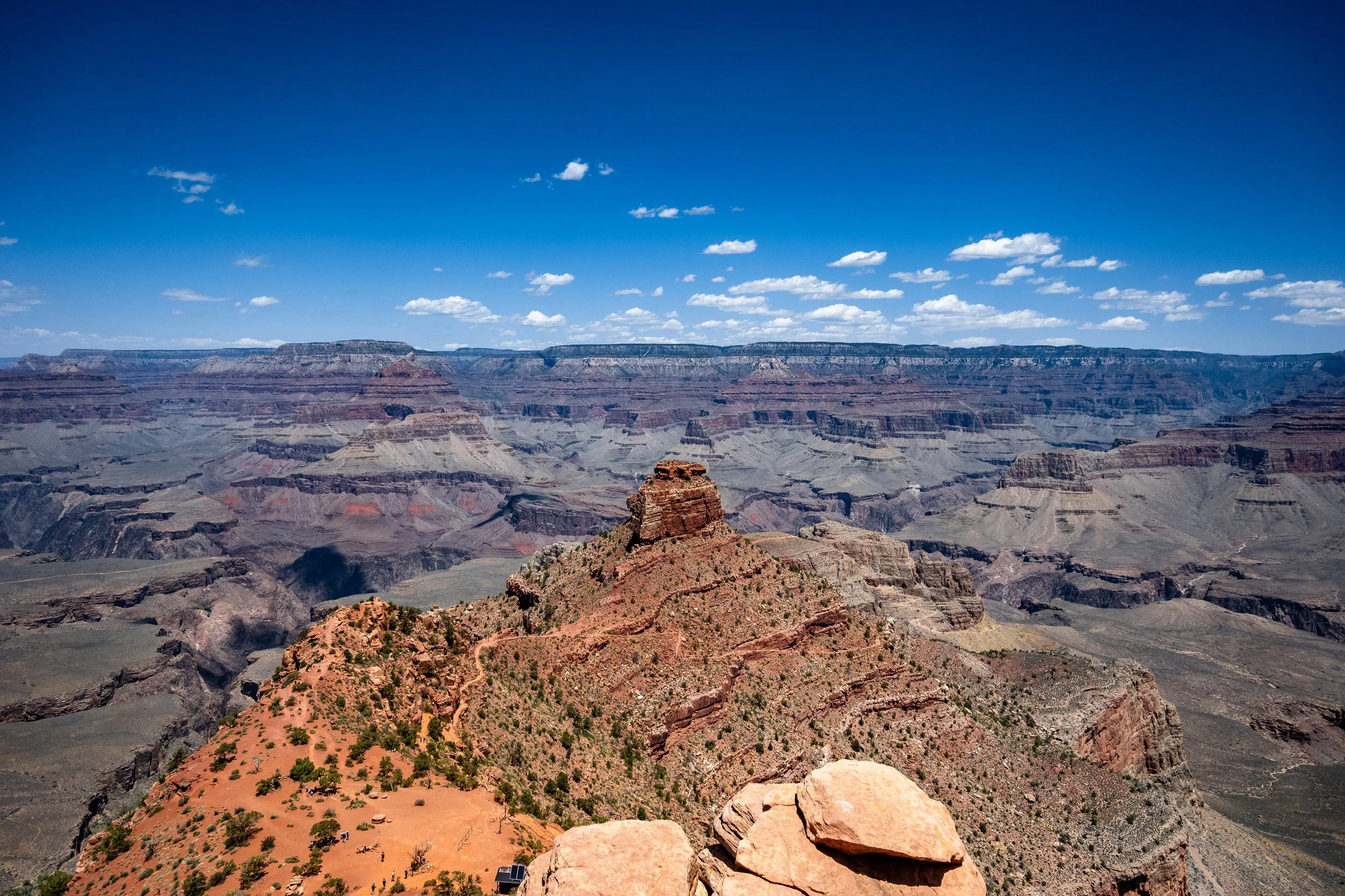 View of the Grand Canyon with layered rock formations under a bright blue sky with scattered clouds.