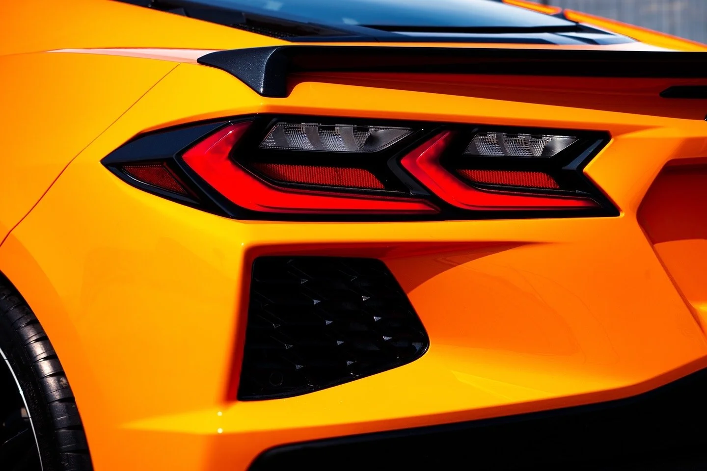 Close-up of a bright orange sports car's rear end, showing its sleek tail light and rear design.