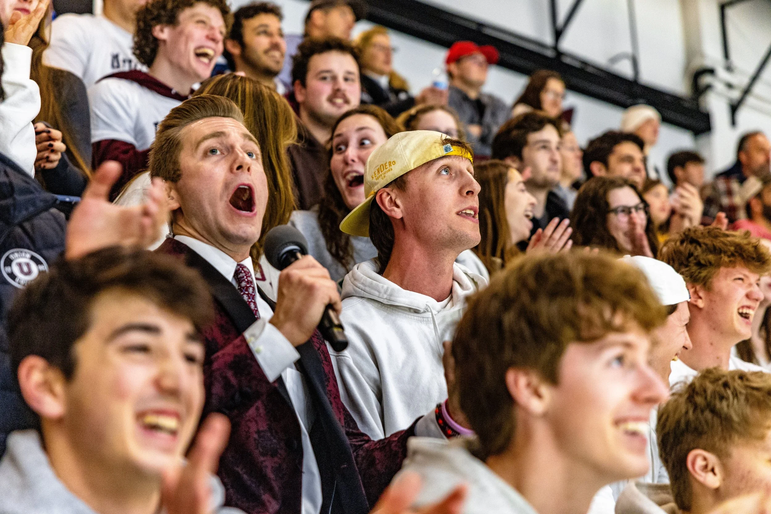 A group of young people attending a lively event, showing various reactions including excitement, surprise, and joy, with some clapping and smiling in an indoor setting.