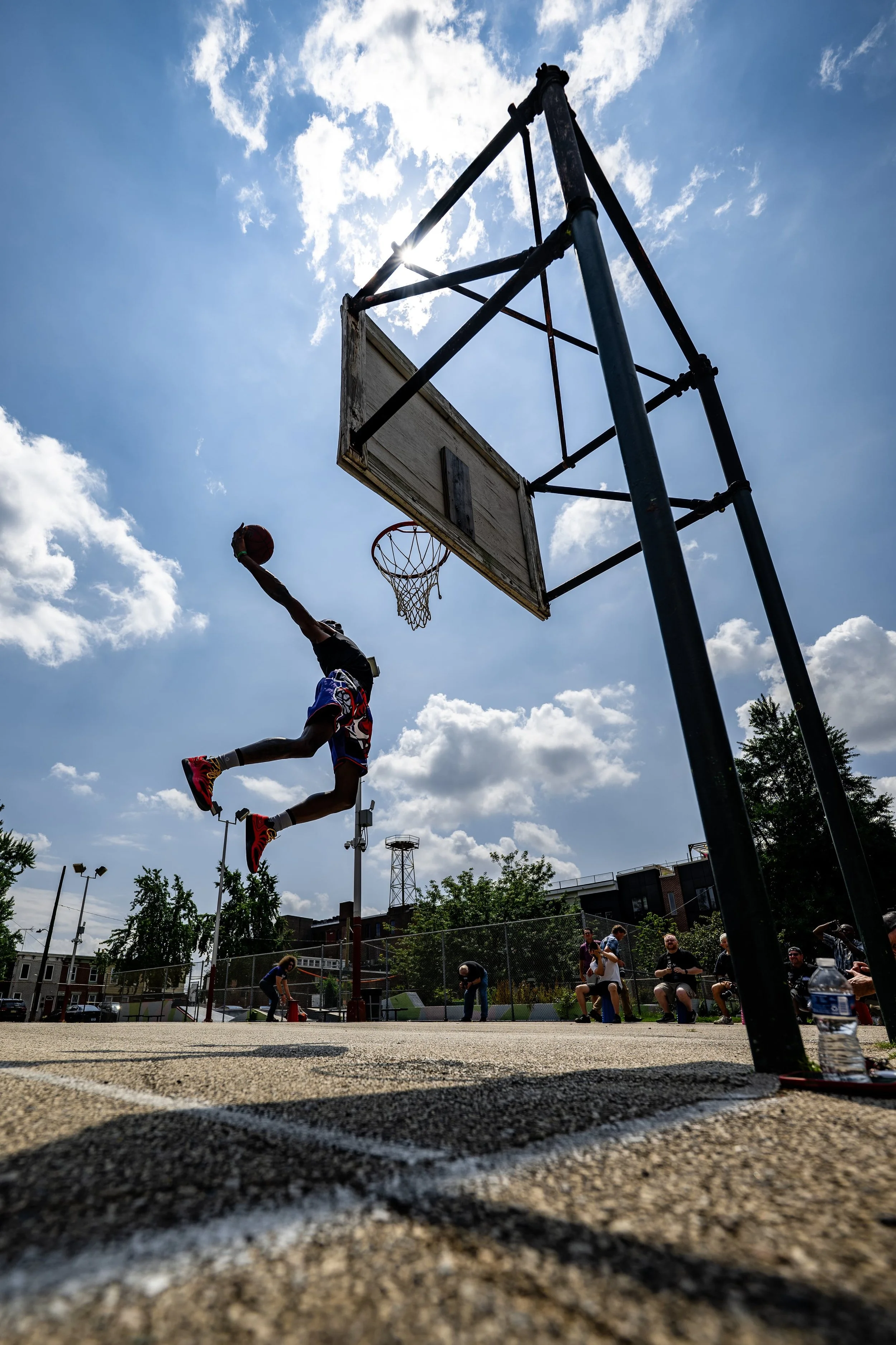 A person dunking a basketball at an outdoor court during daytime with a partly cloudy sky.
