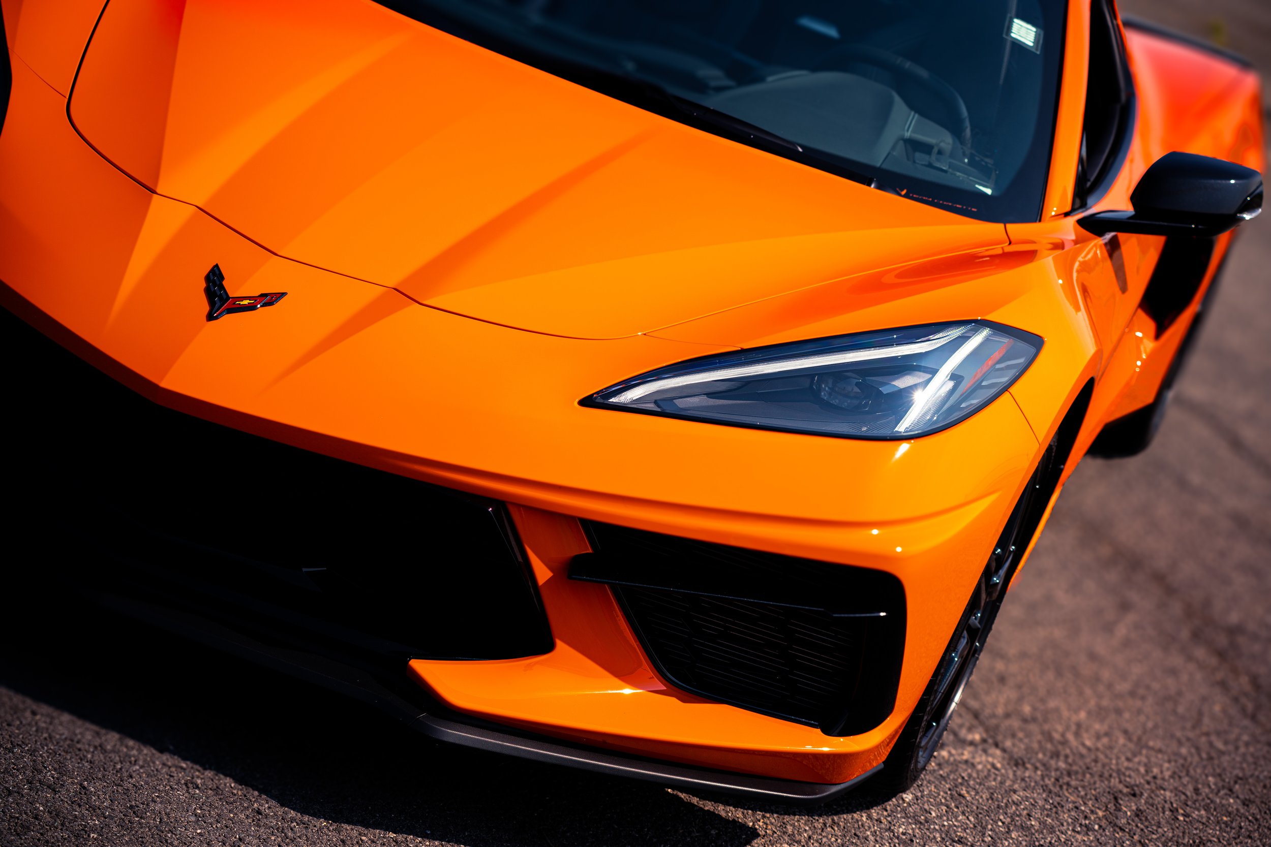 Close-up of the front end of an orange Chevrolet Corvette sports car with sleek headlights and Chevrolet logo on the hood.