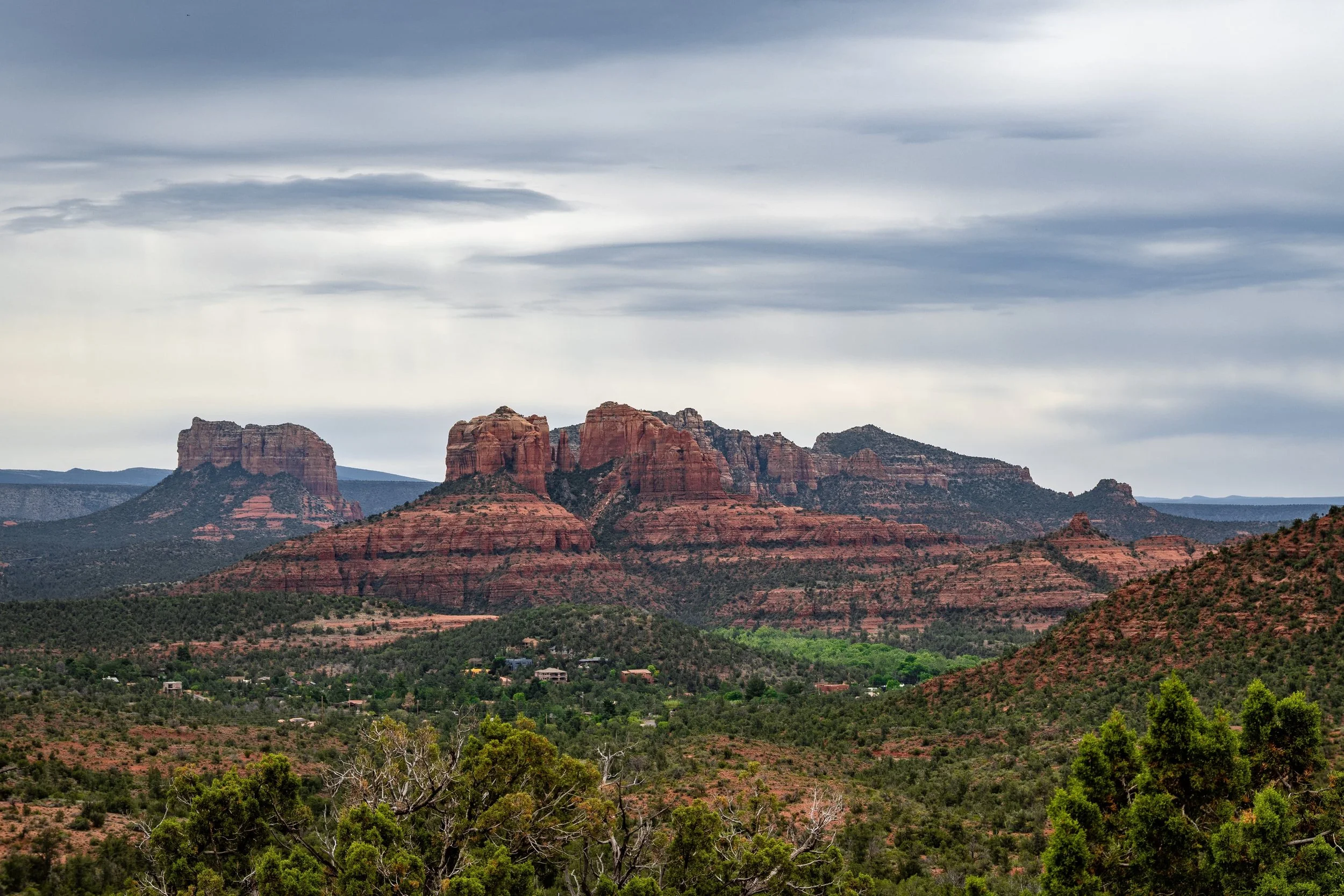 Scenic view of red rock formations and green vegetation under a cloudy sky, characteristic of a desert landscape.
